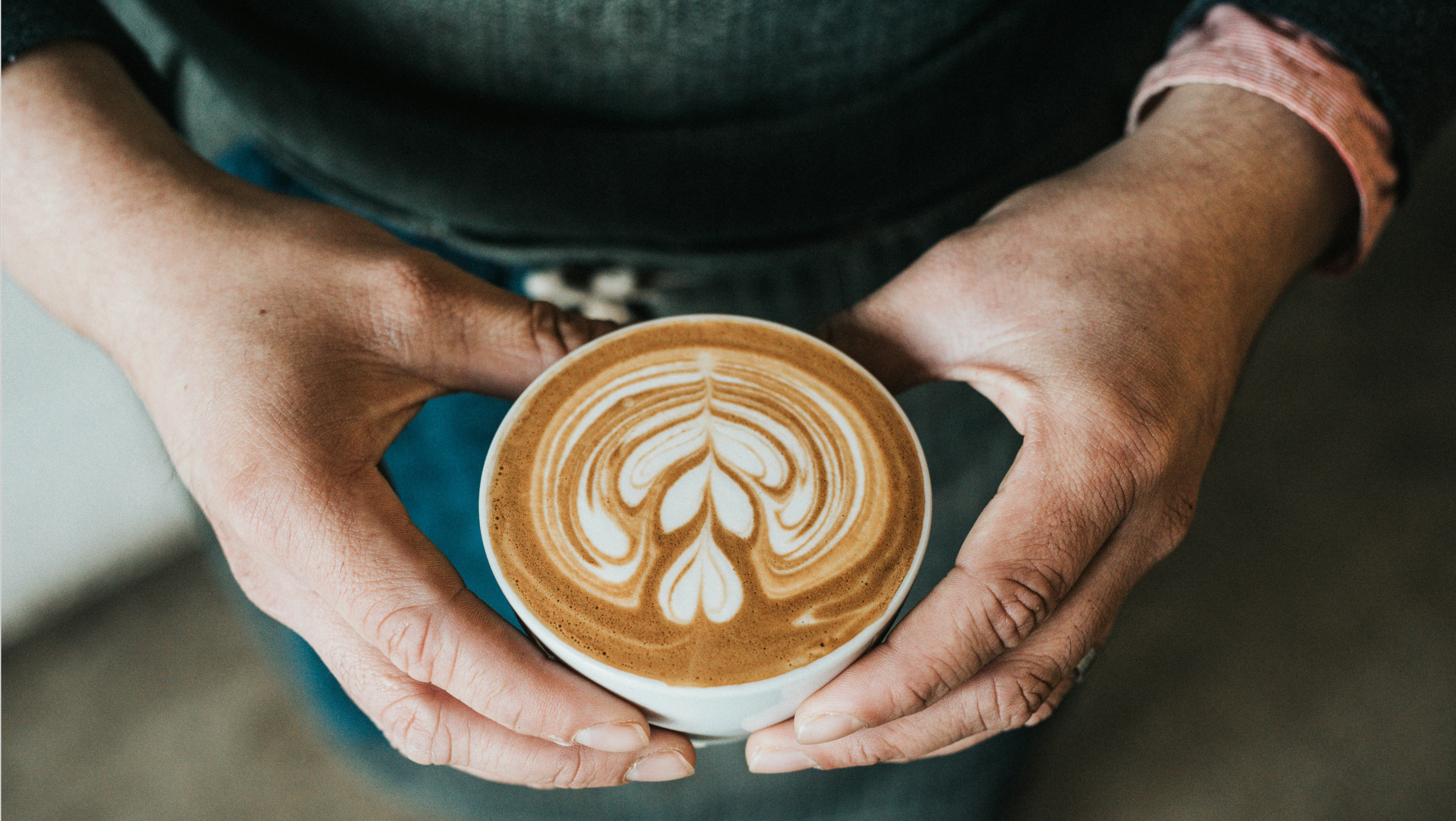 Two hands holding a cup of Kolkin coffee with latte art.